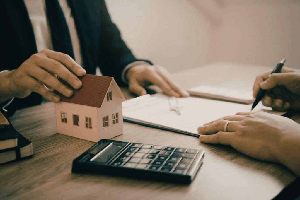 Real estate agent discussing a home sale with a small house model, calculator, and paperwork
